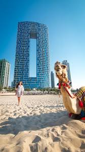 a camel lying at sand and a girl walking with background of dubai skyline